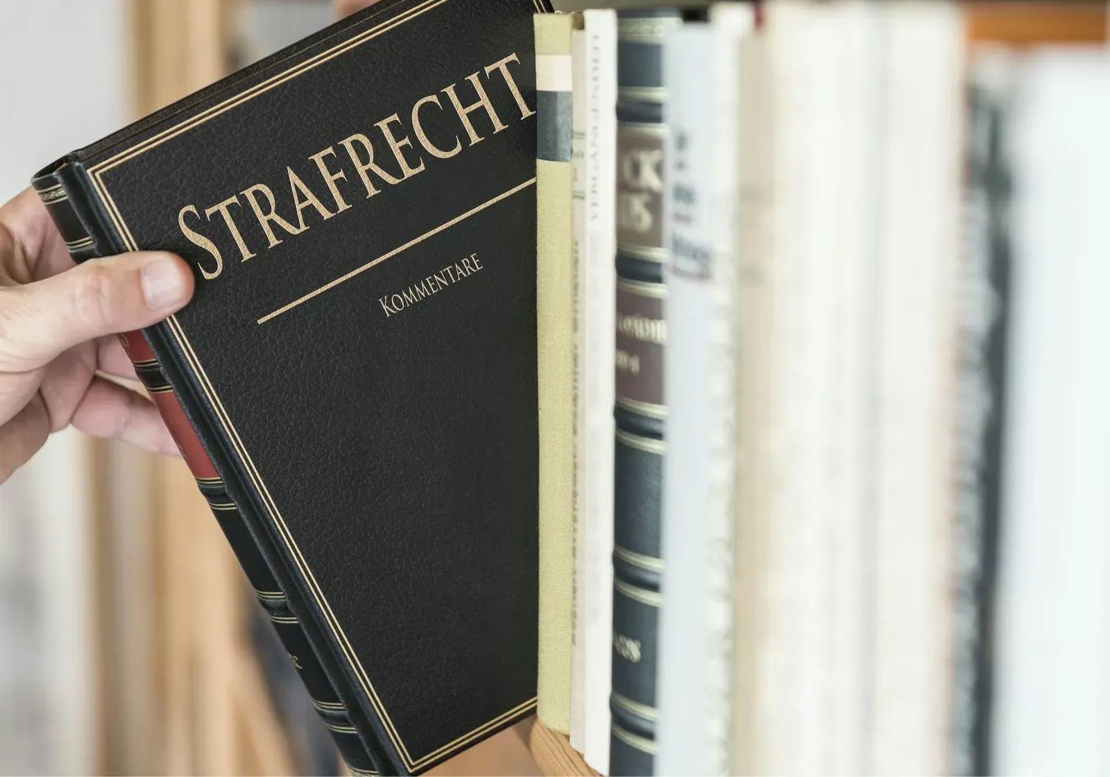 Hand zieht einen Gesetzeskommentar mit der Aufschrift Strafrecht aus einem Buecherregal, Symbolbild fuer Wirtschaftsstrafrecht der Kanzlei Rechtsanwalt Hermann Kaufmann